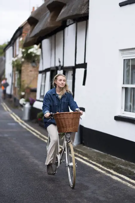 Young blond woman cycling down a village street.