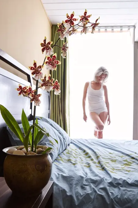 Attractive mature Caucasian woman in her bedroom, standing by the window. 