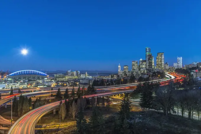 The city skyline of Seattle at night, road and bridge, downtown buildings lit up in moonlight.