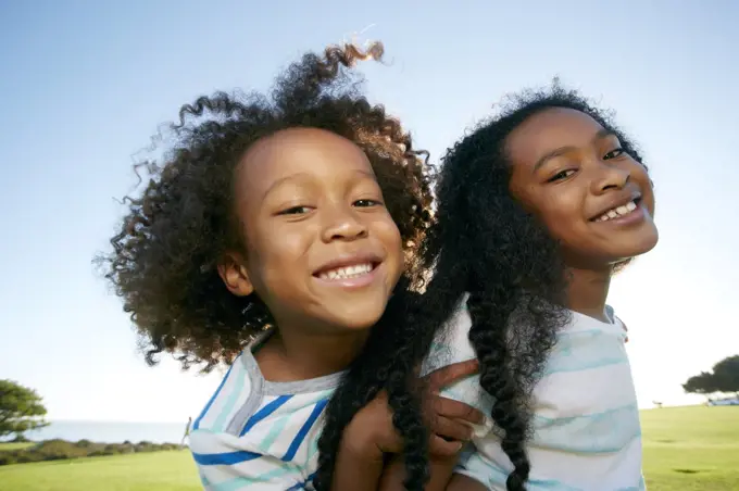 Young mixed race girl giving her younger brother a piggyback lift