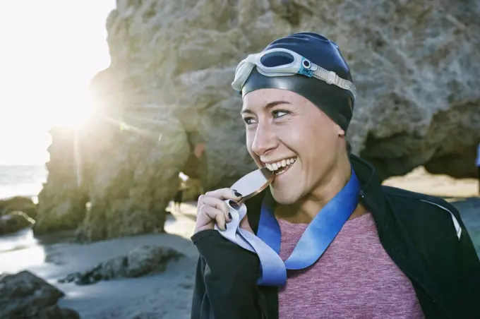 Young woman, triathlete in jacket biting a large medal with her teeth, a winner