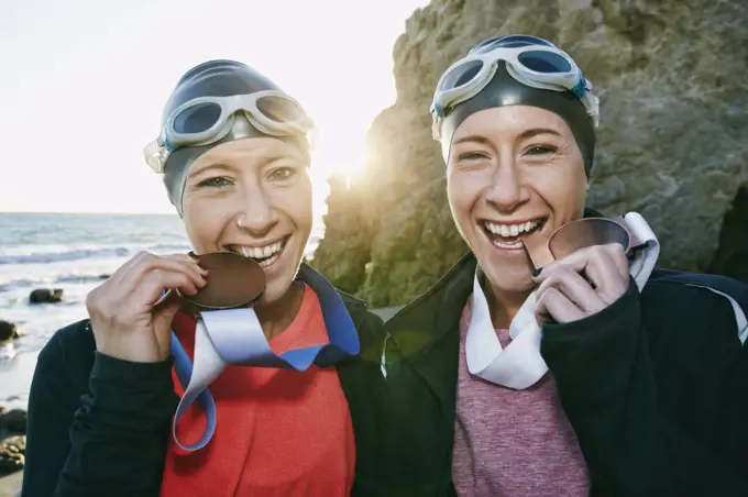 Two sisters, triathletes in swimhats and goggles wearing their large medals, winners. 