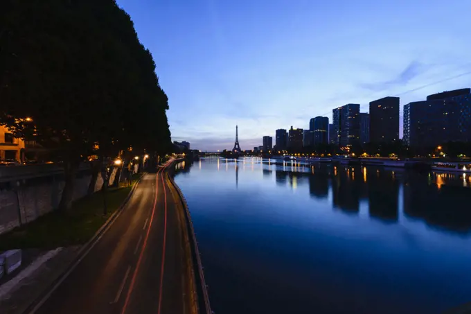 View along the River Seine to the Eiffel tower, the river embankment, and the city at dusk, reflections on the water. 