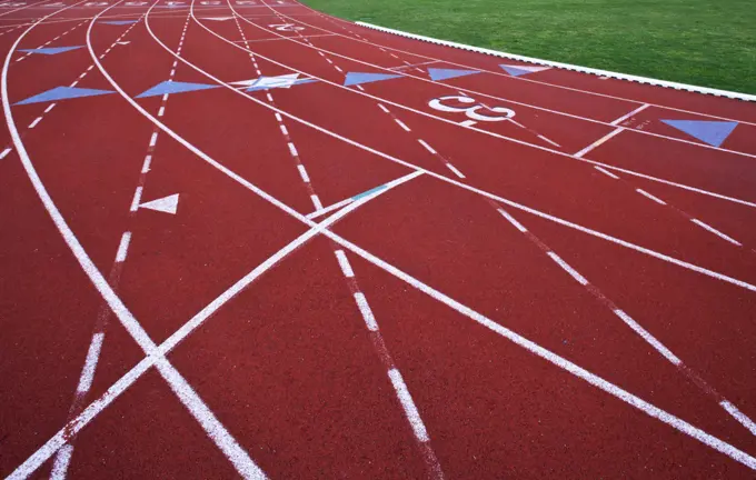 A red artificial surface running track. A sports ground. Painted marked lines for lanes.