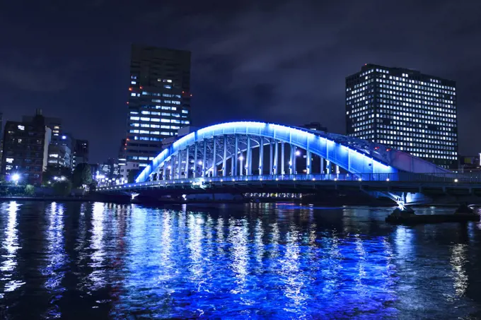 The city of Tokyo at night, the Sumida River and Eitai bridge, lit up, with high rise buildings. 