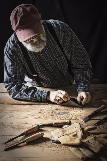 A man working in a reclaimed lumber yard workshop. Holding tools and sanding knotted and uneven piece of wood. Pine Plains, New York, USA