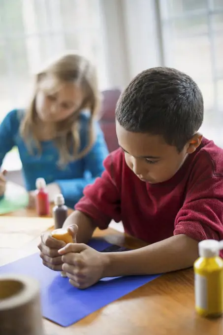 Children in a family home.  Two children sitting at the table, using paint and paper to create decorations. Woodland Valley, New York, USA