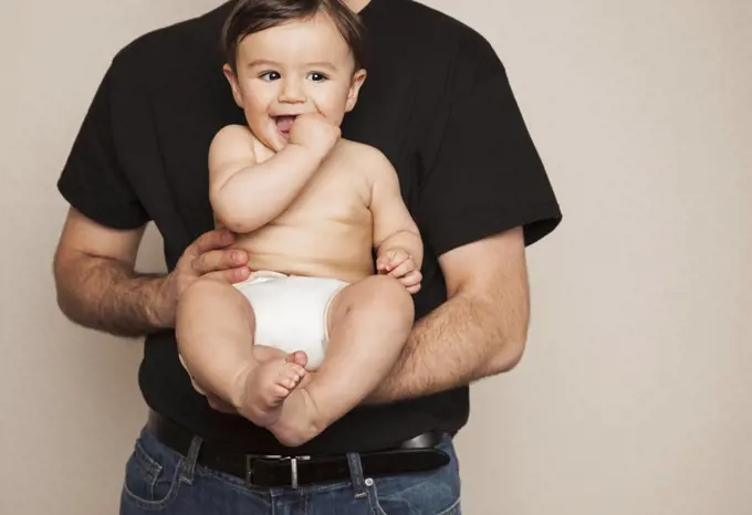 A young boy wearing cloth diapers being held by his father in his arms.  Santa Fe, New Mexico, USA