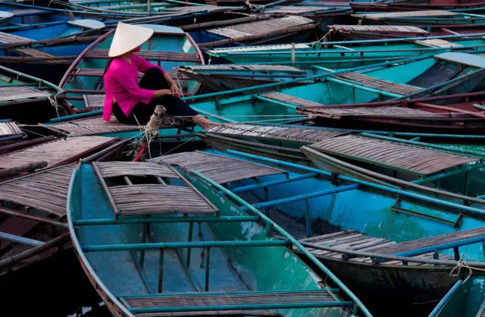 Lost in thought, a woman sits amidst a raft of boats. Ninh Binh, Vietnam Ninh Binh, Vietnam