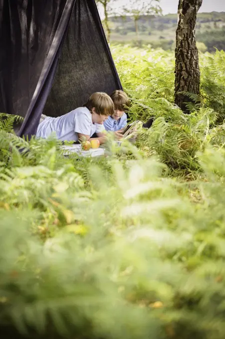 Two boys camping in the New Forest, lying under a canvas shelter. Hampshire, England. 08/06/2013