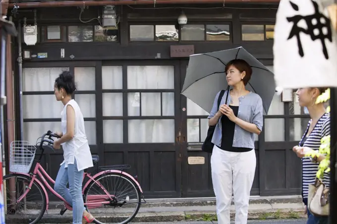 Woman standing outdoors, holding an umbrella.