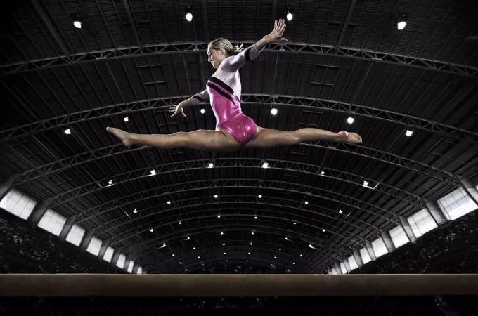 A young woman gymnast performing on the beam, balancing on a narrow piece of apparatus.