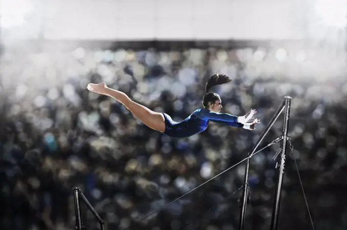 A female gymnast, a young woman performing on the parallel bars, in mid flight reaching towards the top bar.