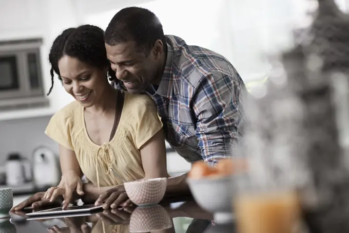 A man and woman, couple in ther kitchen both looking at a digital tablet.