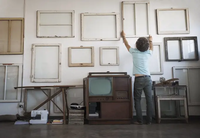 Loft decor. A man hanging framed picture canvases on a wall.