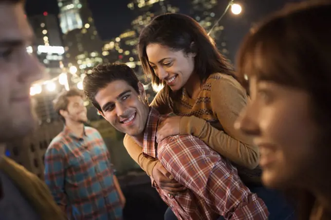 A group of men and women at a rooftop party with a view over the city.