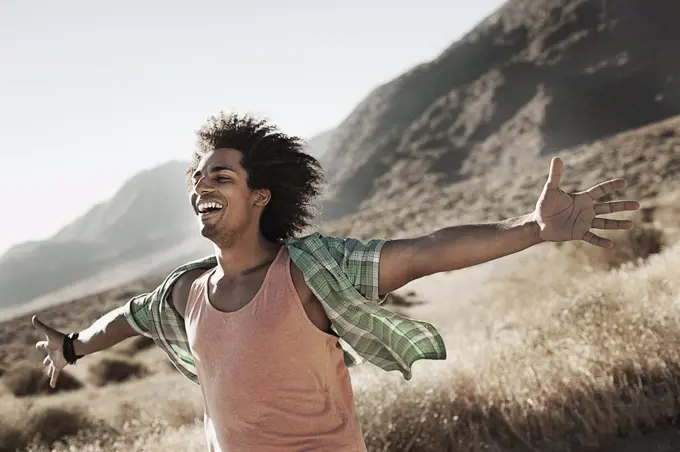 A man standing with arms outstretched in a gesture of freedom and excitement, leaning into the breeze.