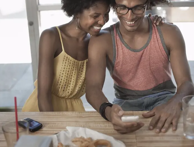 A young couple sitting together hugging, laughing at a screen text or picture on a smart phone.