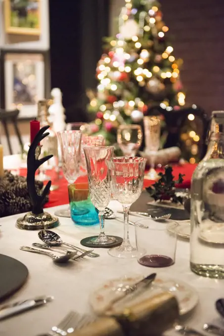 A table laid for a Christmas meal, with silver and crystal glasses and a Christmas tree in the background.