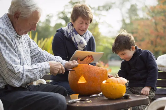 Two adults and a small child with large pumpkins, creating pumpkin lanterns for Halloween.