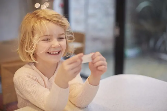 A young girl laughing and looking at a small piece of paper, a joke from a Christmas cracker.