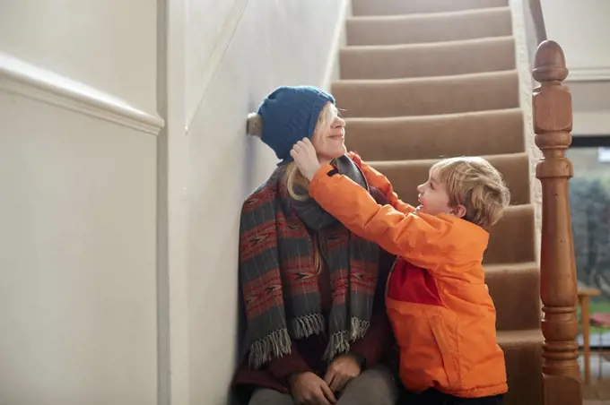 A boy pulling a hat over his mother's eyes.