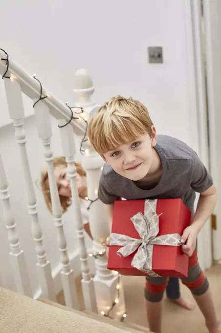 Christmas morning in a family home. Two children on the stairs carrying presents.