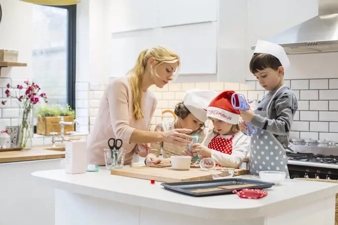 A woman and three children working together, making a gingerbread house, and icing the gingerbread.