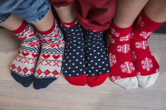 Three pairs of children's feet in bright patterned Christmas socks.