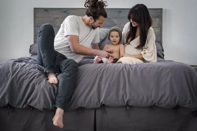 A young couple and their young son sitting together on their bed.