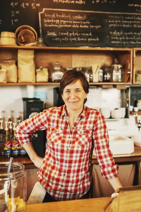 A woman in a coffee shop behind the counter, smiling, business owner.