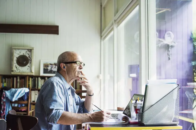 A man seated at a desk at home, working on a laptop computer.