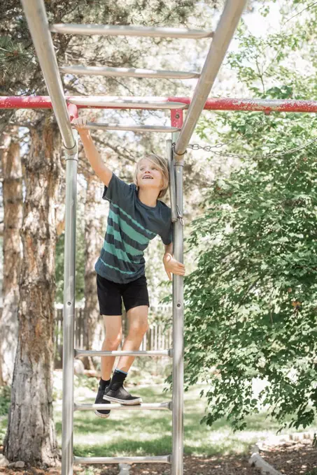 Blond boy on a climbing frame in a garden.