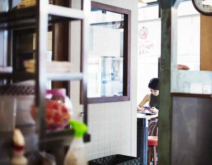 The ramen noodle shop. A woman sitting in a cafe, view through a door.