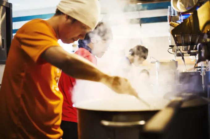 The ramen noodle shop. A chef stirring a huge pot of noodles cooking.