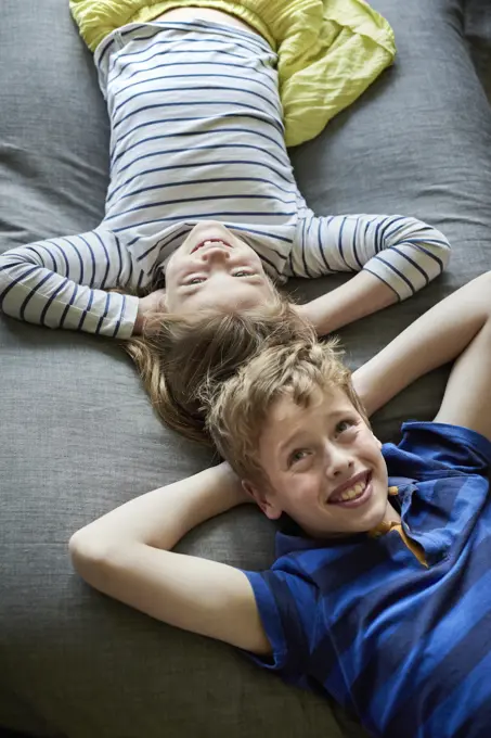 A family home.  A boy and girl lying on the sofa with their heads close together. View from above.