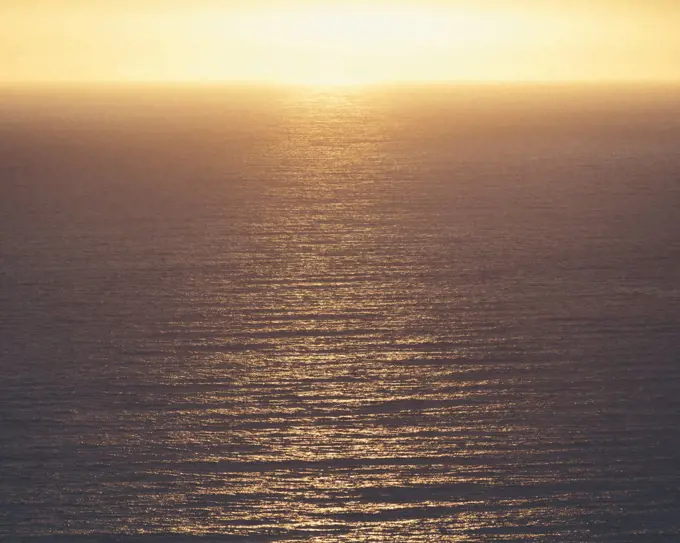 View from the land over the ocean, to the horizon. The sun resting on the horizon and light reflecting off the water.