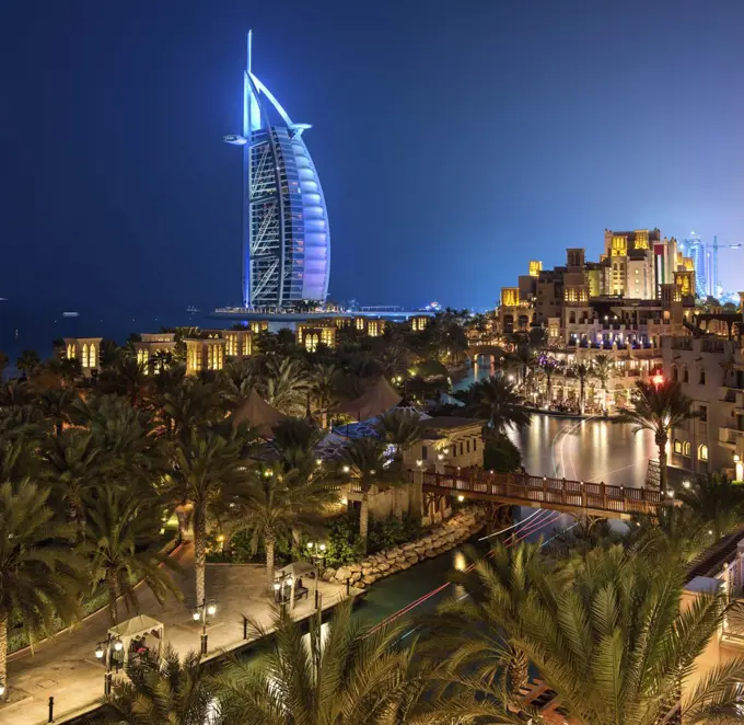 View of illuminated Burj Al Arab skyscraper in Dubai, United Arab Emirates at dusk.