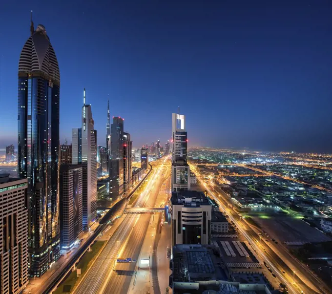 Cityscape of Dubai, United Arab Emirates at dusk, with skyscrapers lining illuminated street.