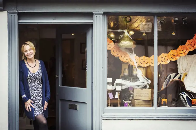 A woman standing in the doorway of her pop up interior design shop with a window display of objects.