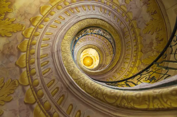 Low angle view of spiral staircase decorated with murals of golden Acanthus flowers and ornamental borders.