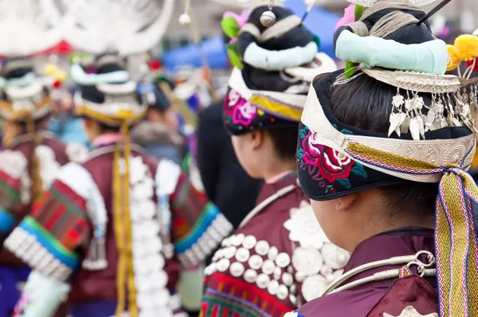 Rear view of girls wearing colourful traditional Chinese costumes and headdresses dancing at a festival.