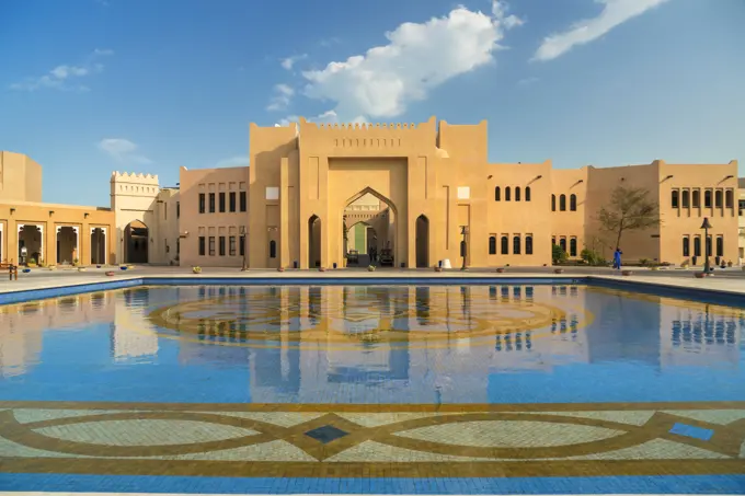 Facade of Middle Eastern building, pond with blue and golden mosaic tiles in foreground.