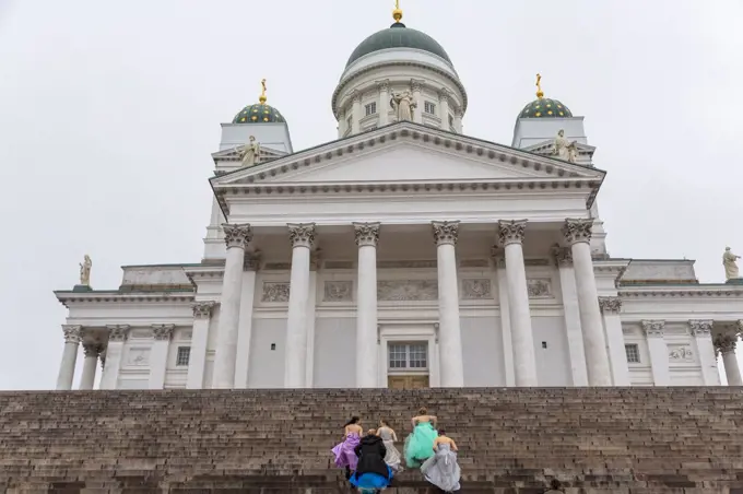 Group of women in colourful dresses walking up the steps of the Lutheran Cathedral in Helsinki, Finland.