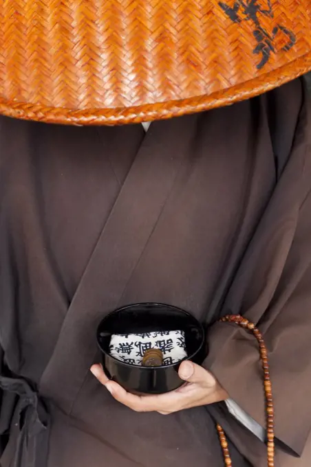 Close up of Japanese monk wearing traditional clothing holding alms bowl.