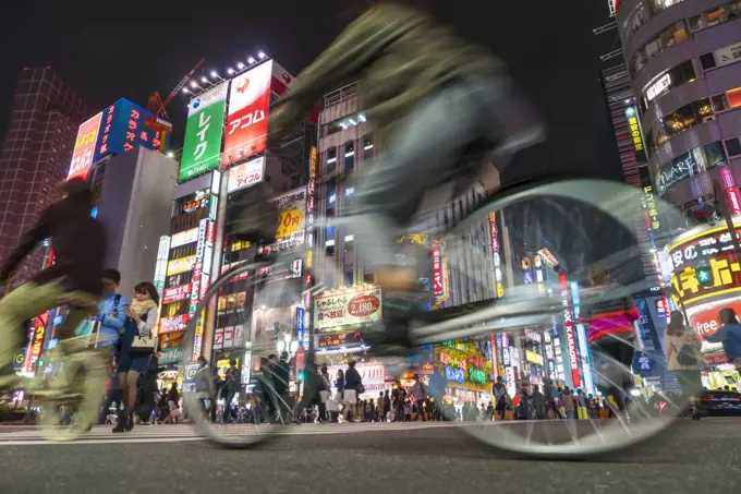 Surface view of cyclists driving on urban street at night illuminated skyscrapers and neon advertising.