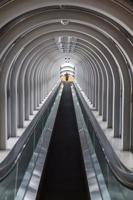 Interior view of contemporary building with escalator running across glass atrium with arched ceiling.