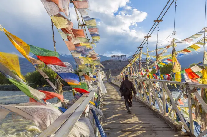 Rear view of man walking across bridge decorated with colourful prayer flags.