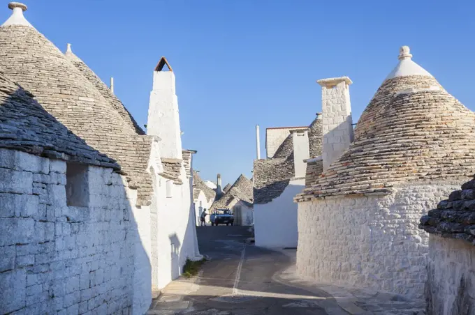 Traditional white washed round stone houses with conical roofs lining Mediterranean street.