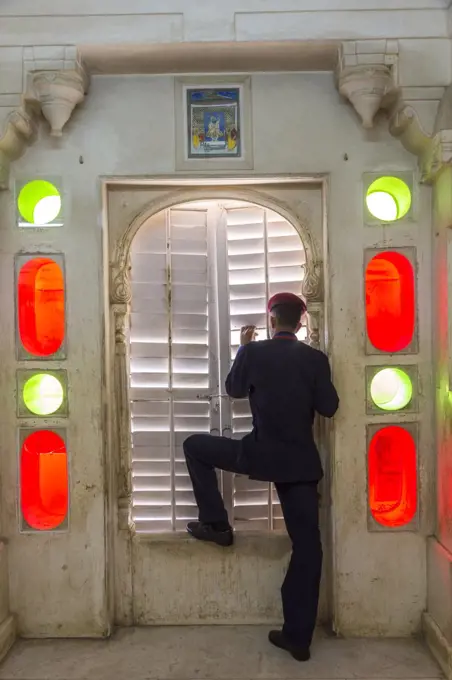 Rear view of man wearing uniform standing at a closed door, looking through shutters.